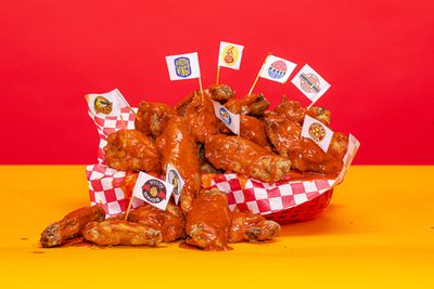 An image of a basket full of wings over a red and yellow background. Several wings have a toothpick planted in them connected to a flag with a different made up chicken wing restaurant logo.
