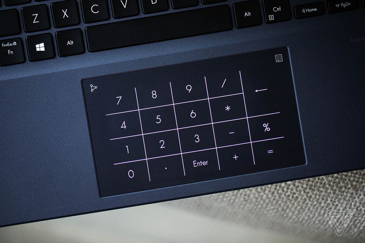 The touchpad of the Asus Vivobook Pro 14 with the numpad illuminated, seen from above on a white fabric surface.
