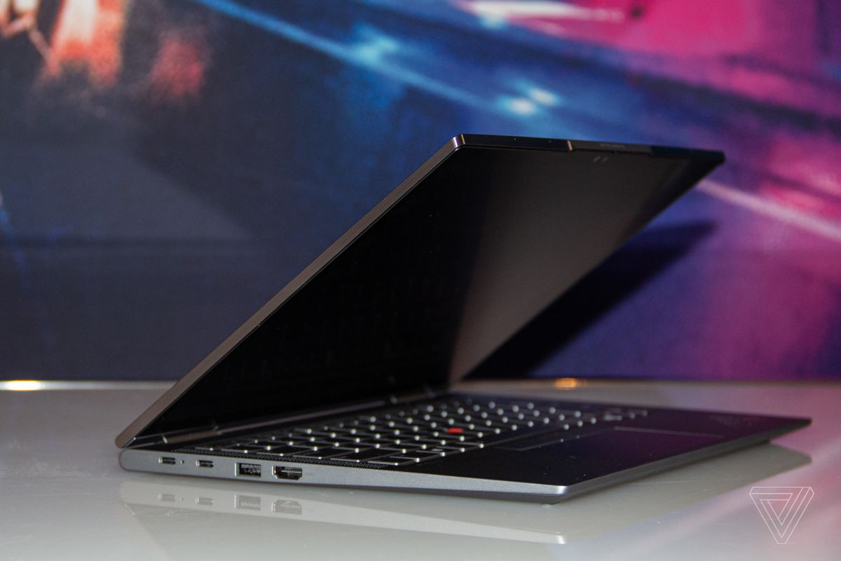 The ThinkPad X1 Yoga angled to the right, half open on a white table with a blue and pink background. The screen is off.