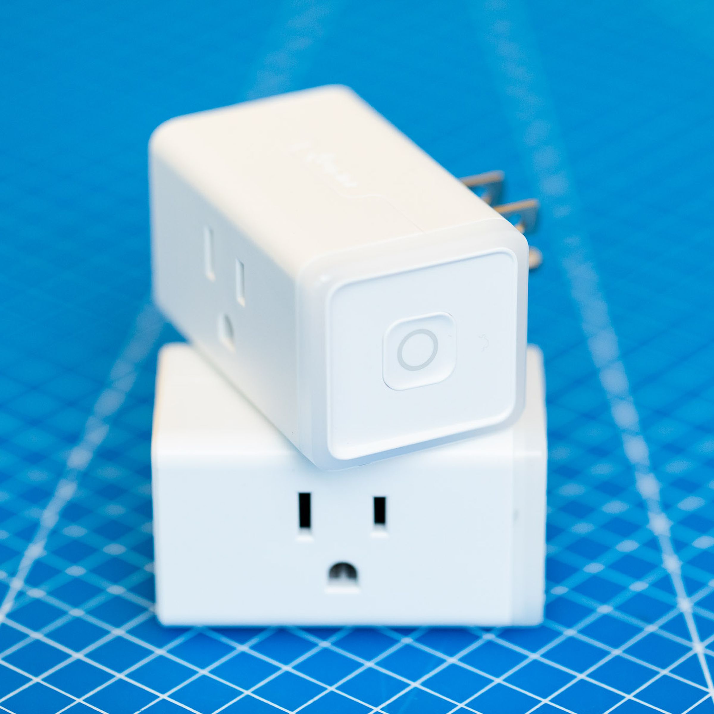 Two TP-Link Kasa KP125M Matter smart plugs stacked on top of each other. They are white rectangular prisms with a three-prong outlet on the front face and three-prong plug on the rear face, TP-Link on the top face, and a power button on the right face. 